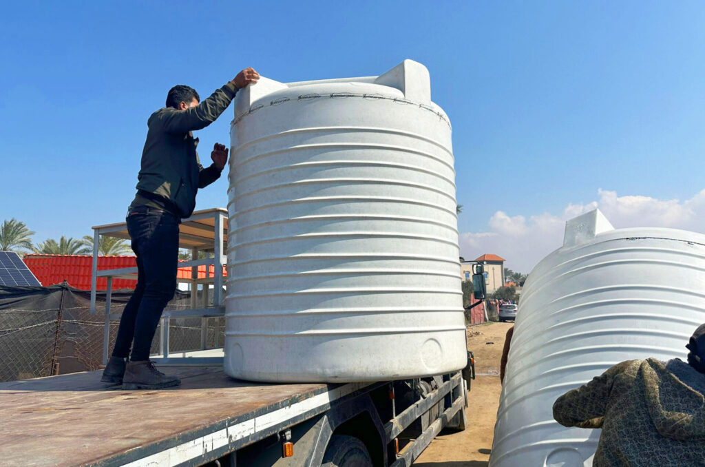 Men unload human-sized water tanks off of a truck.