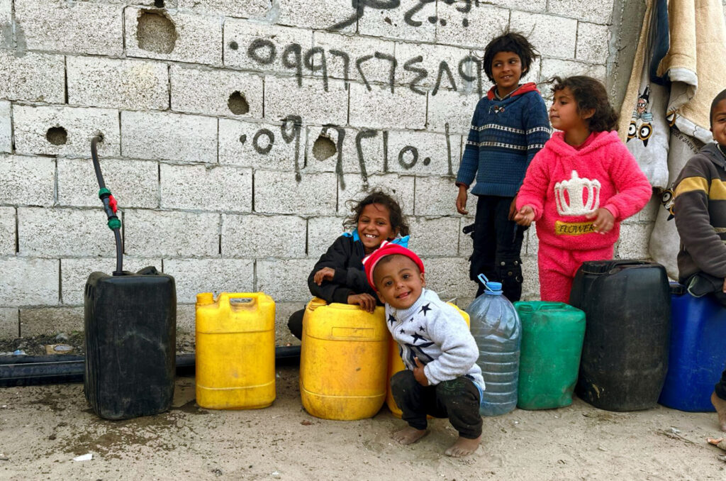Children gather around a water hose to fill their canisters in Gaza.
