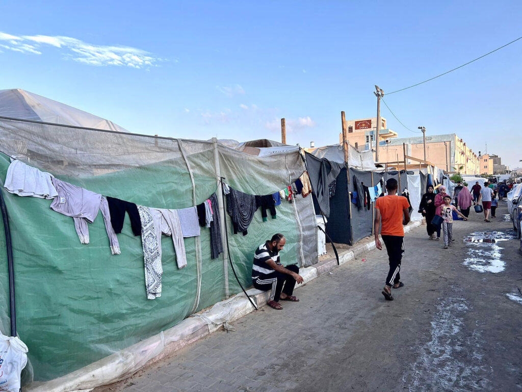 A street in a refugee camp with pooled water and clothes drying from tents.