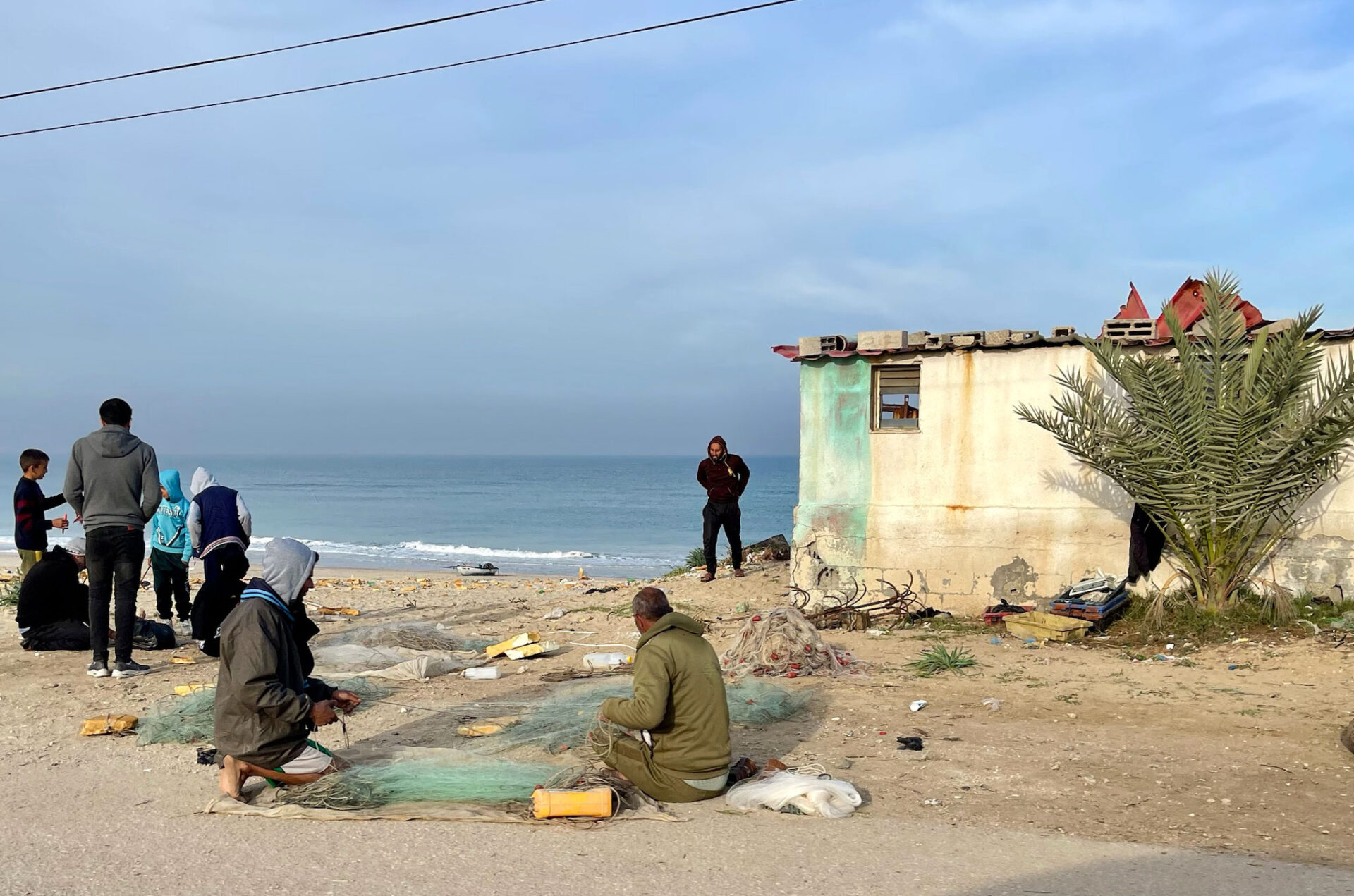 Men work on a fishing net by the sea shore.