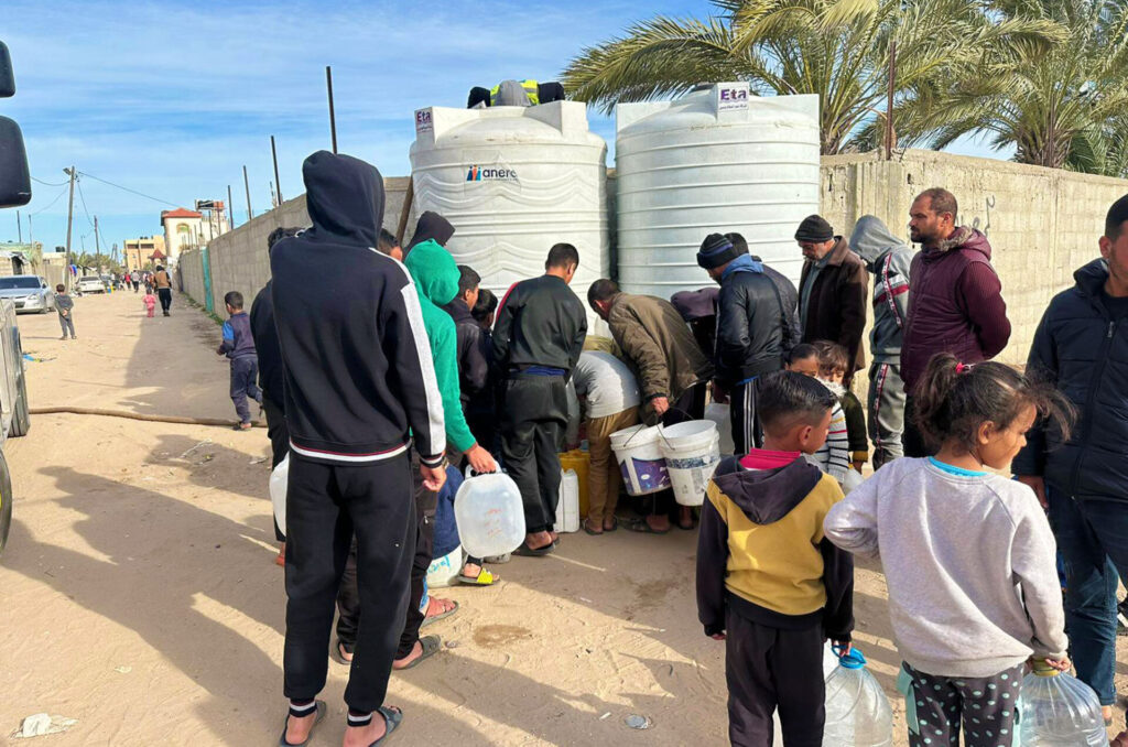 A crowd stands in line to fill water vessels from a water tank in Gaza.