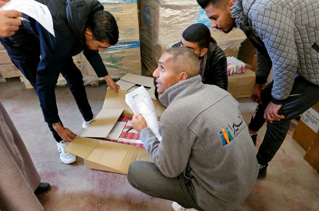 An Anera staff member bends over a box of medicine to distribute it. 