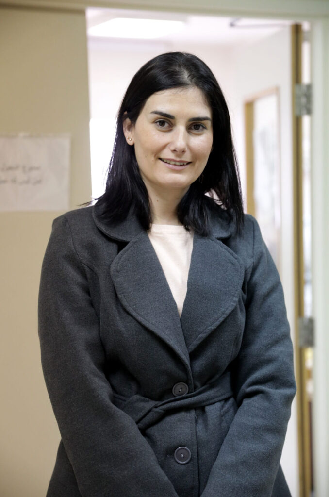 A doctor stands for the camera and smiles inside the hospital they work at.