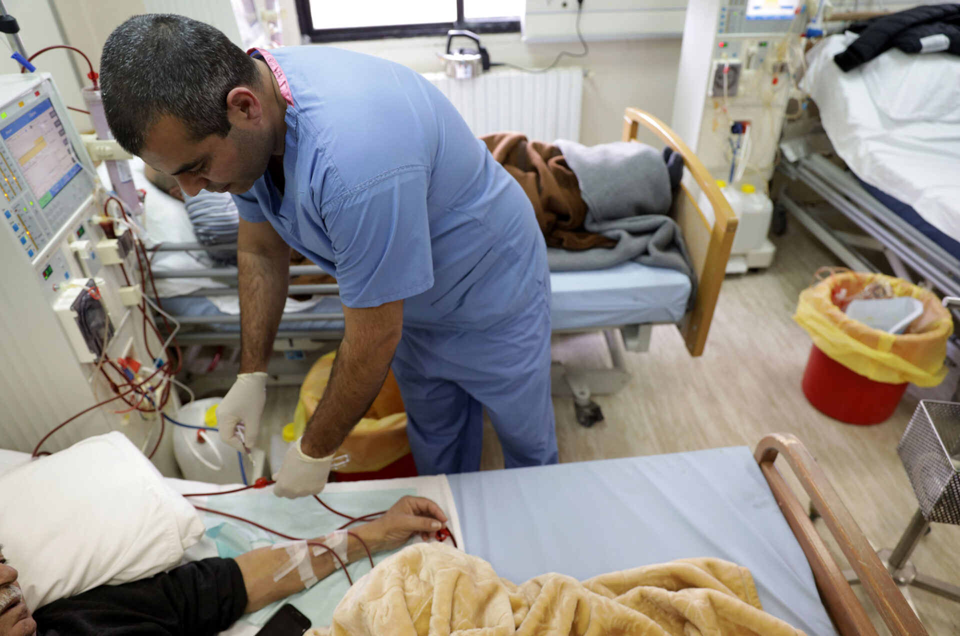 A health care worker leans over a hospital bed to administer anticoagulation medication to a patient.