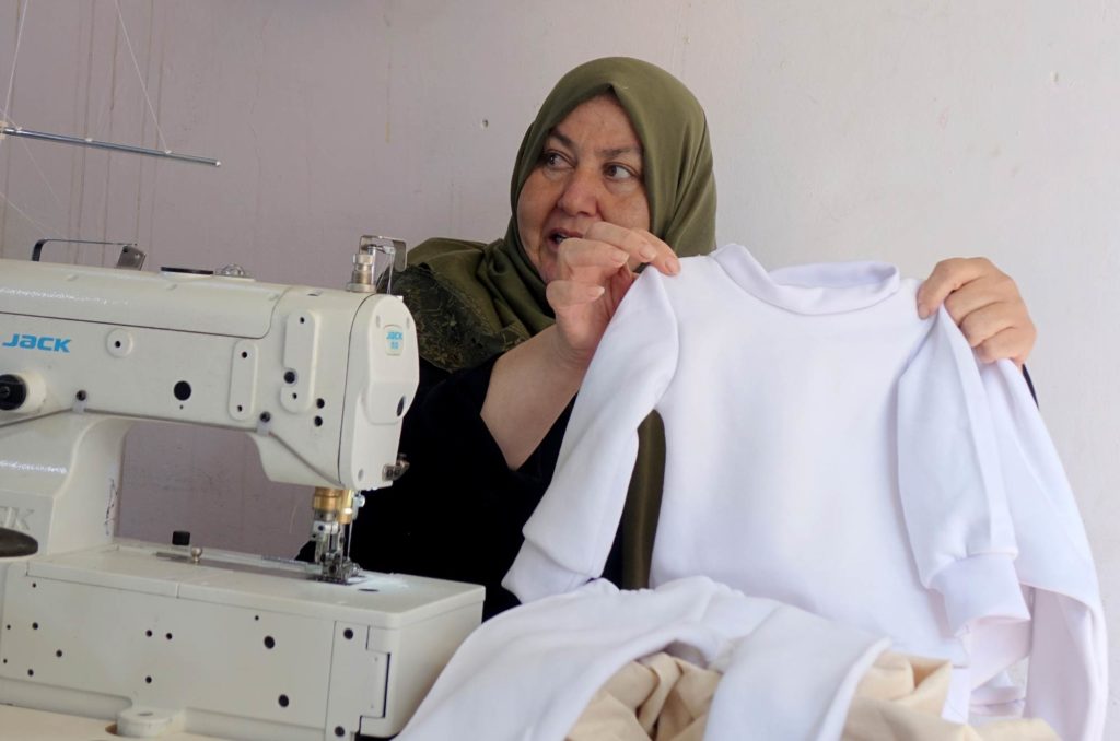 Khayrazan holds up a set of children's clothing that she is currently sewing.