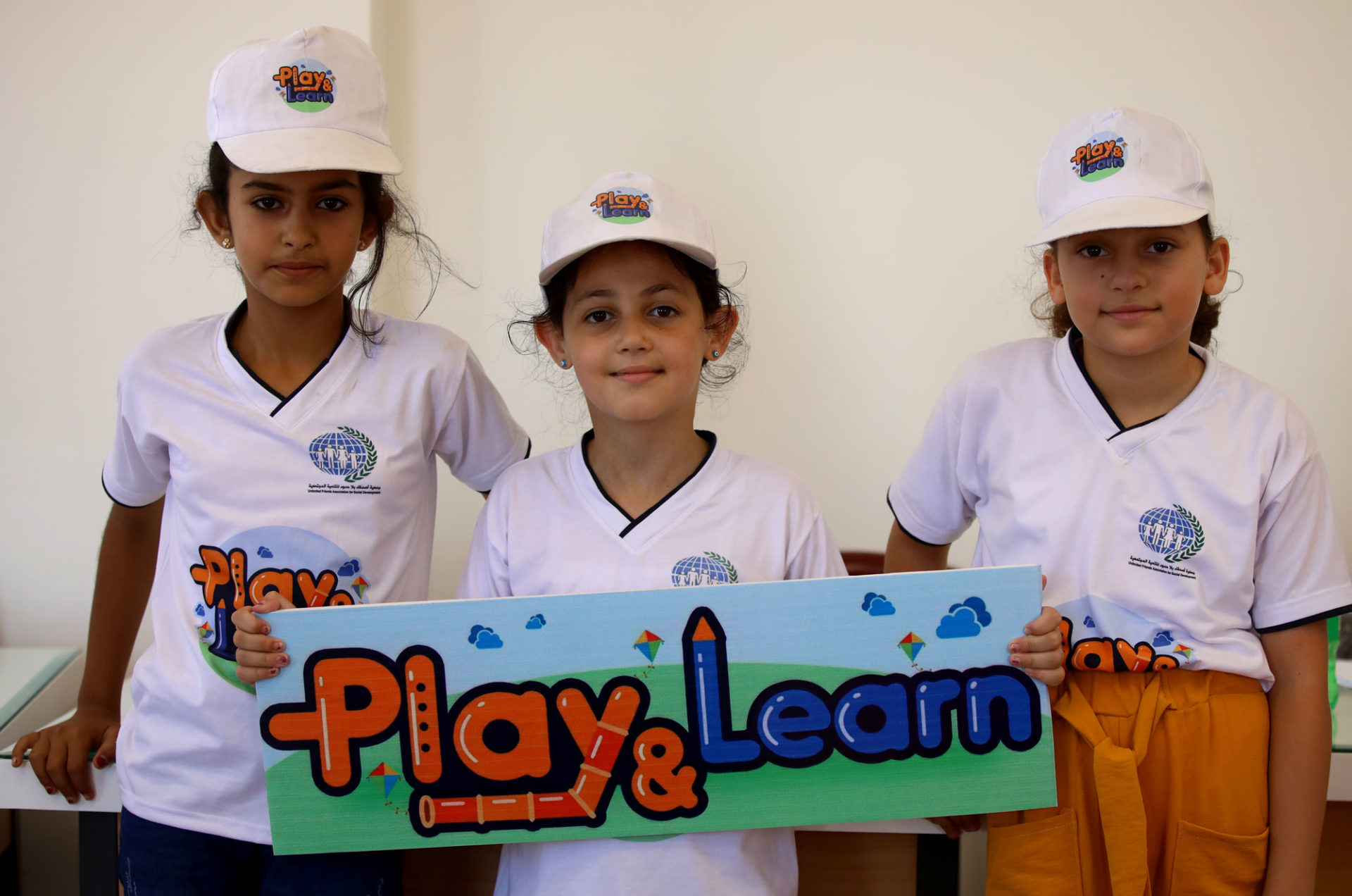 Three children pose with a sign reading 'play & learn'.