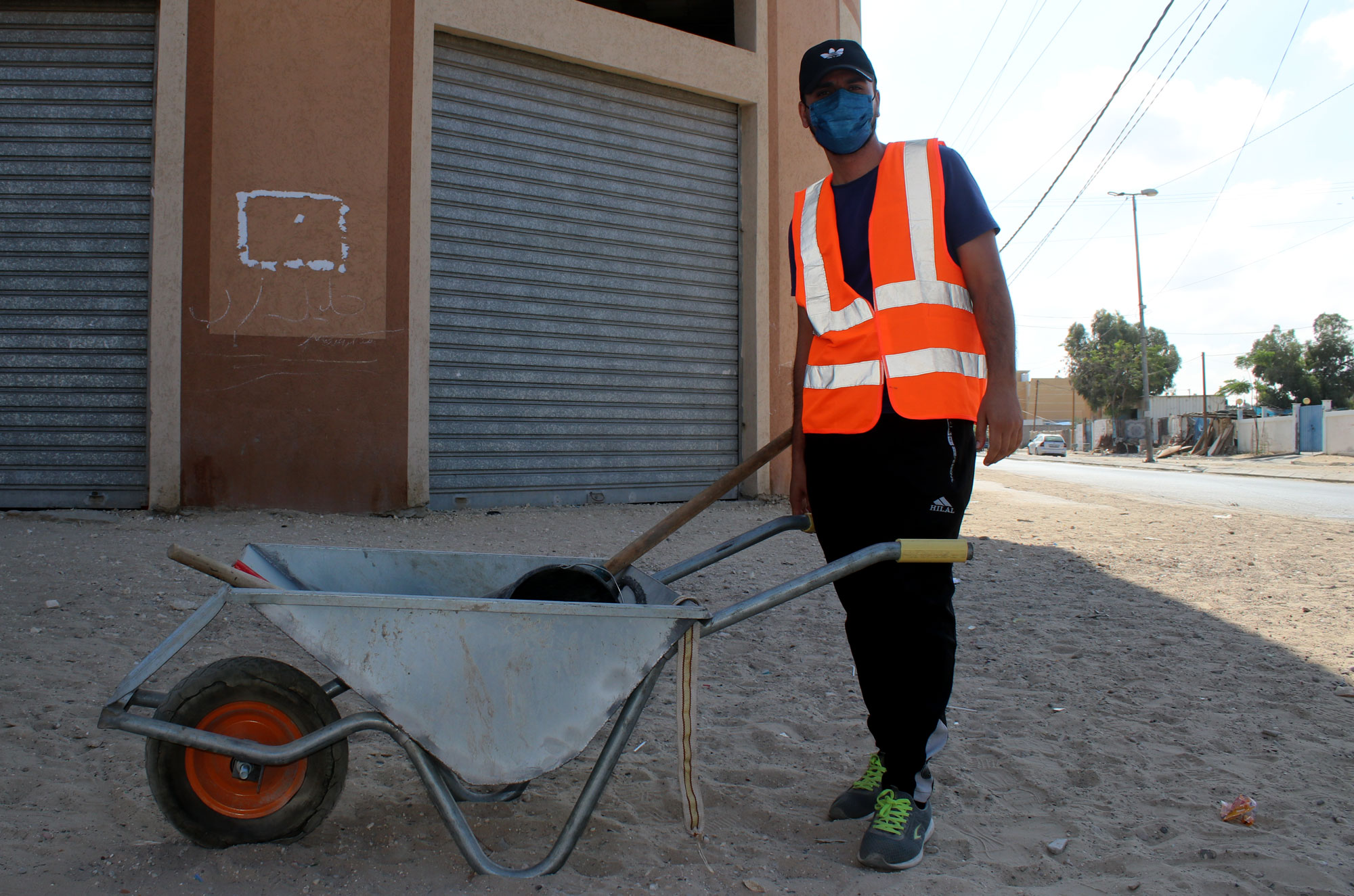 A worker stands with a wheel barrel full of debris.