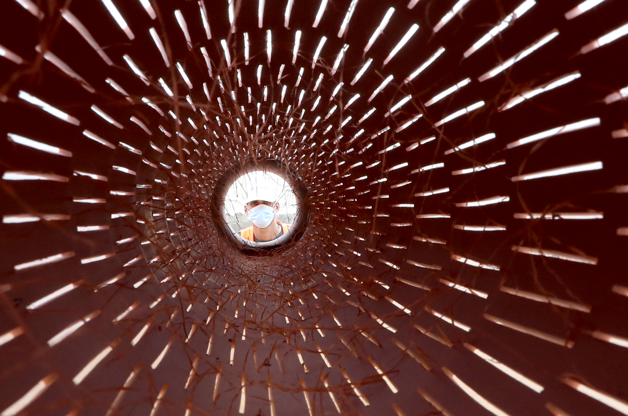 A worker looks at the camera through a segment of pipe.