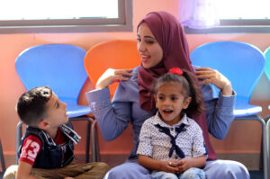Tasneem, one of Anera's early childhood educators, sits with two kindergarteners