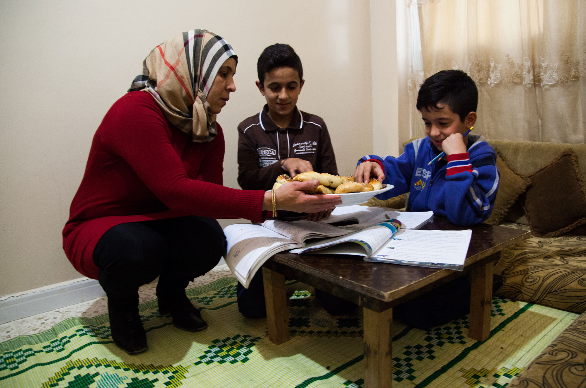 Majida offers freshly baked pastries to her sons while they do their homework.