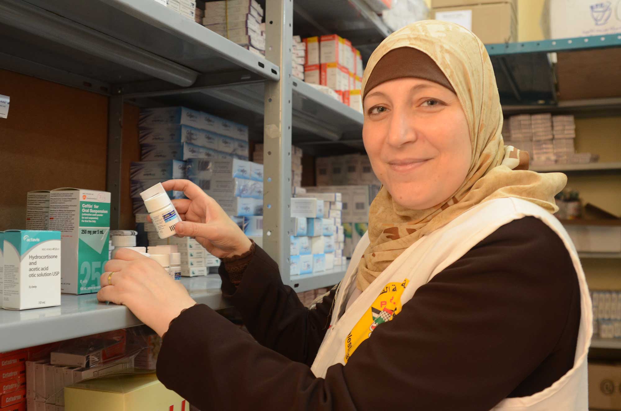 Dima Shawa stocks the shelves of PMRS pharmacy with vital medicines delivered by Anera.
