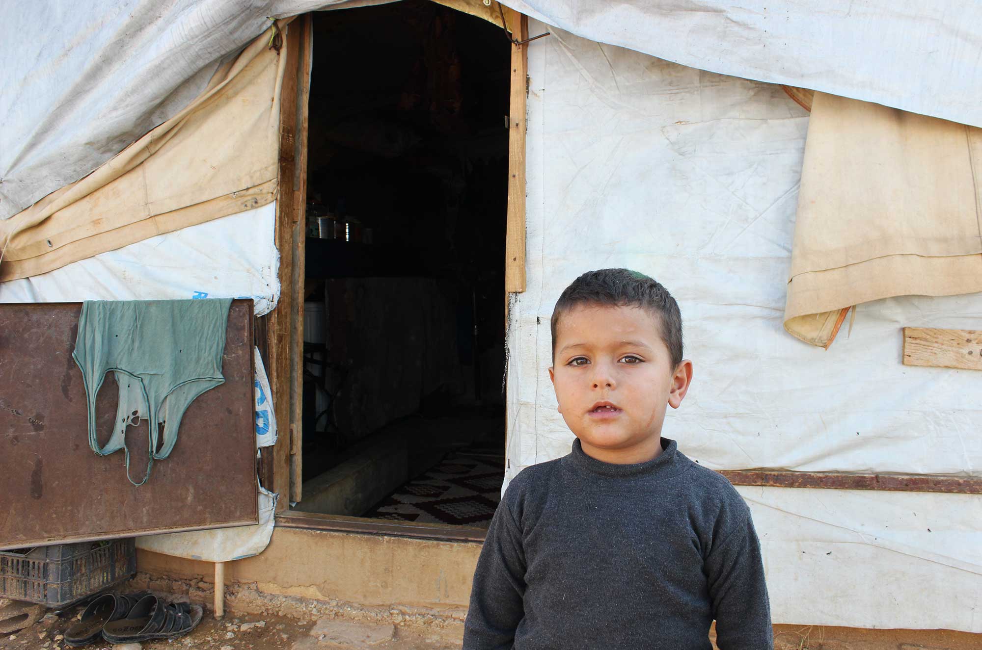 A young Syrian boy stands outside of his temporary home in Lebanon's Akkar region. Akkar is the poorest region in Lebanon & its population has grown by 50% since the start of the Syrian war.