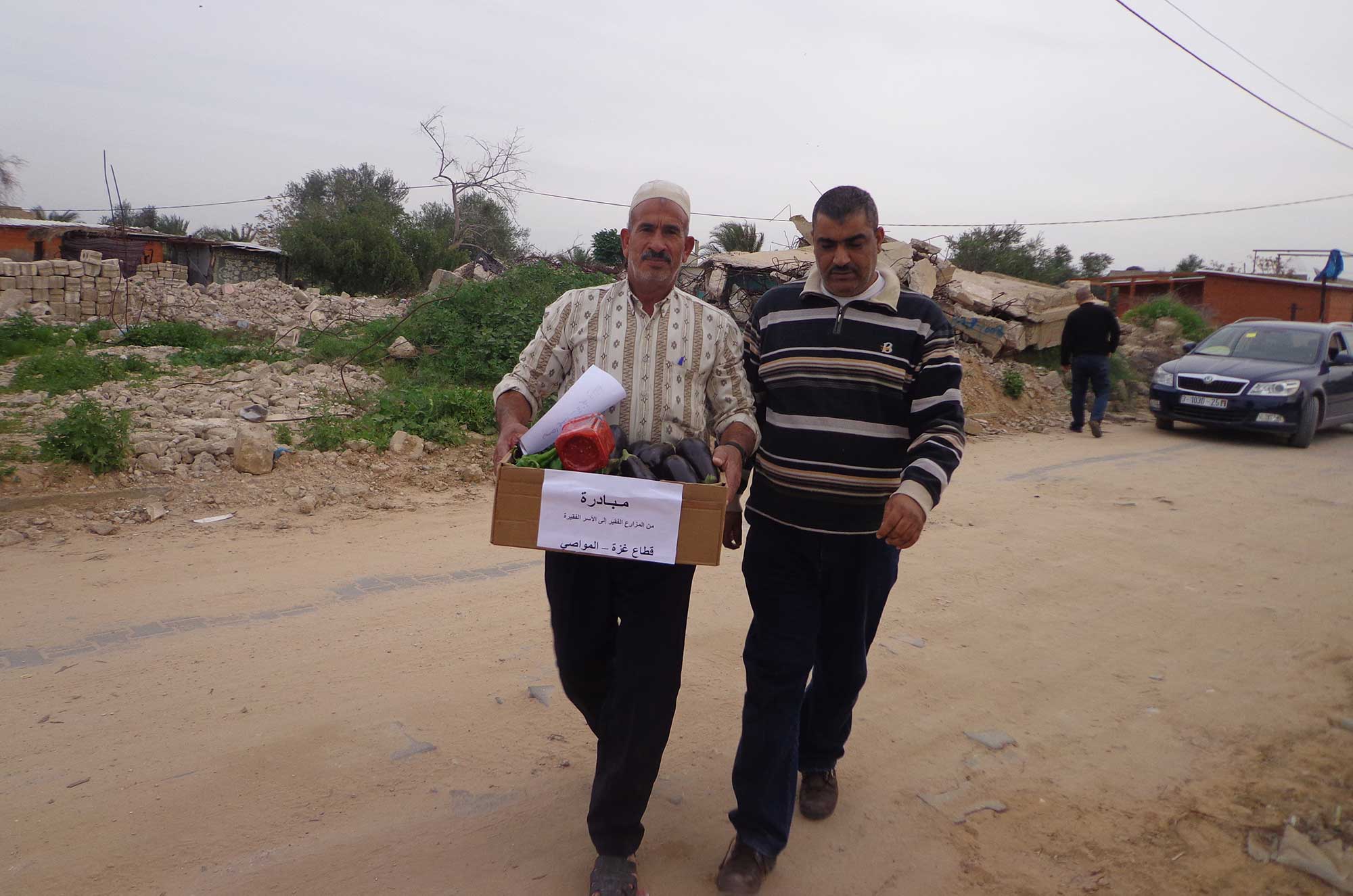 Gaza farmer Ahmed Zoerob (left) walks down the road to a encampment of prefab shelters carrying a box of fresh produce.