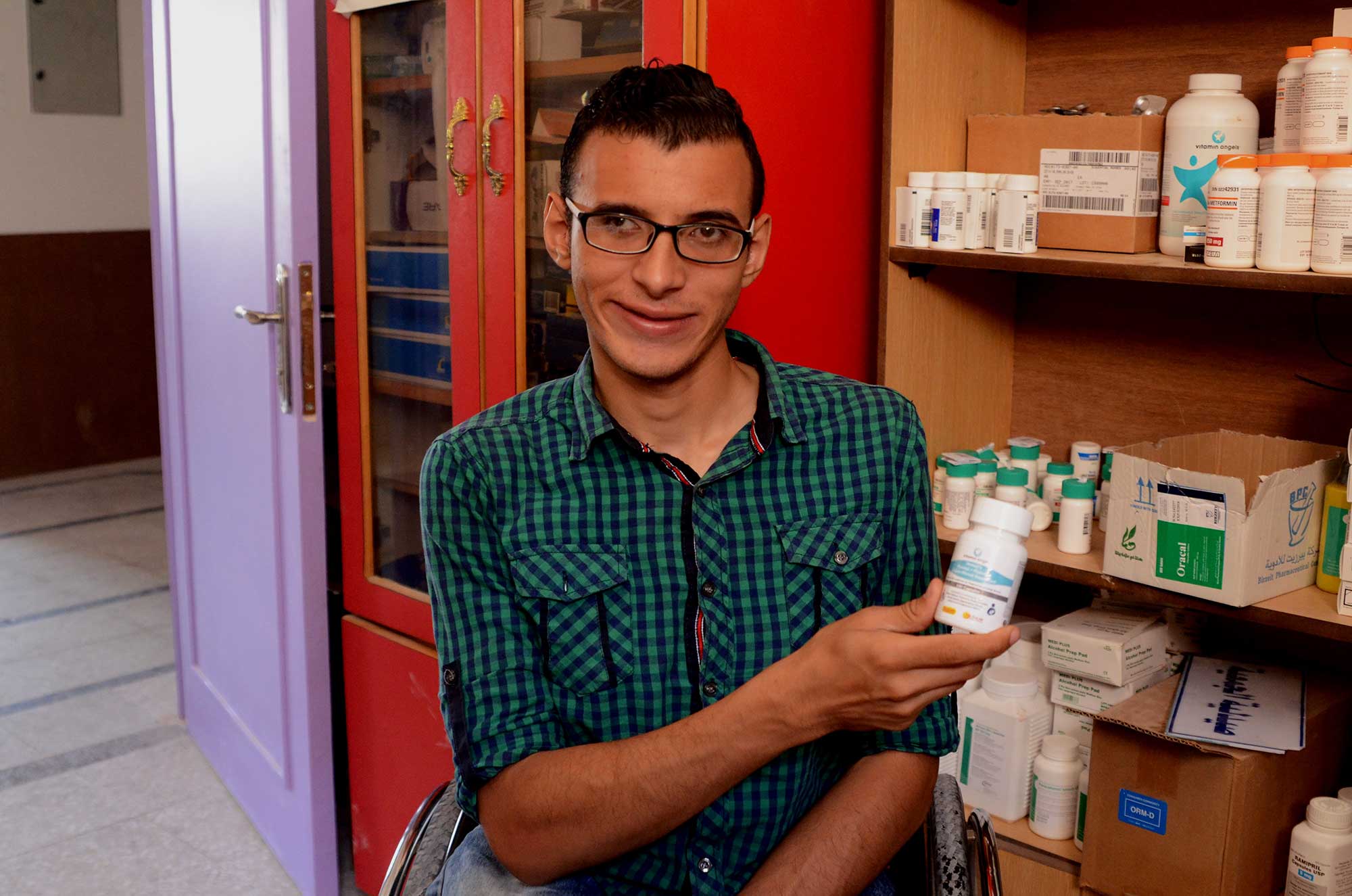 Ali, 19, was left disabled by a car accident. He's holding the medicine he needs to stay healthy, delivered by Anera.