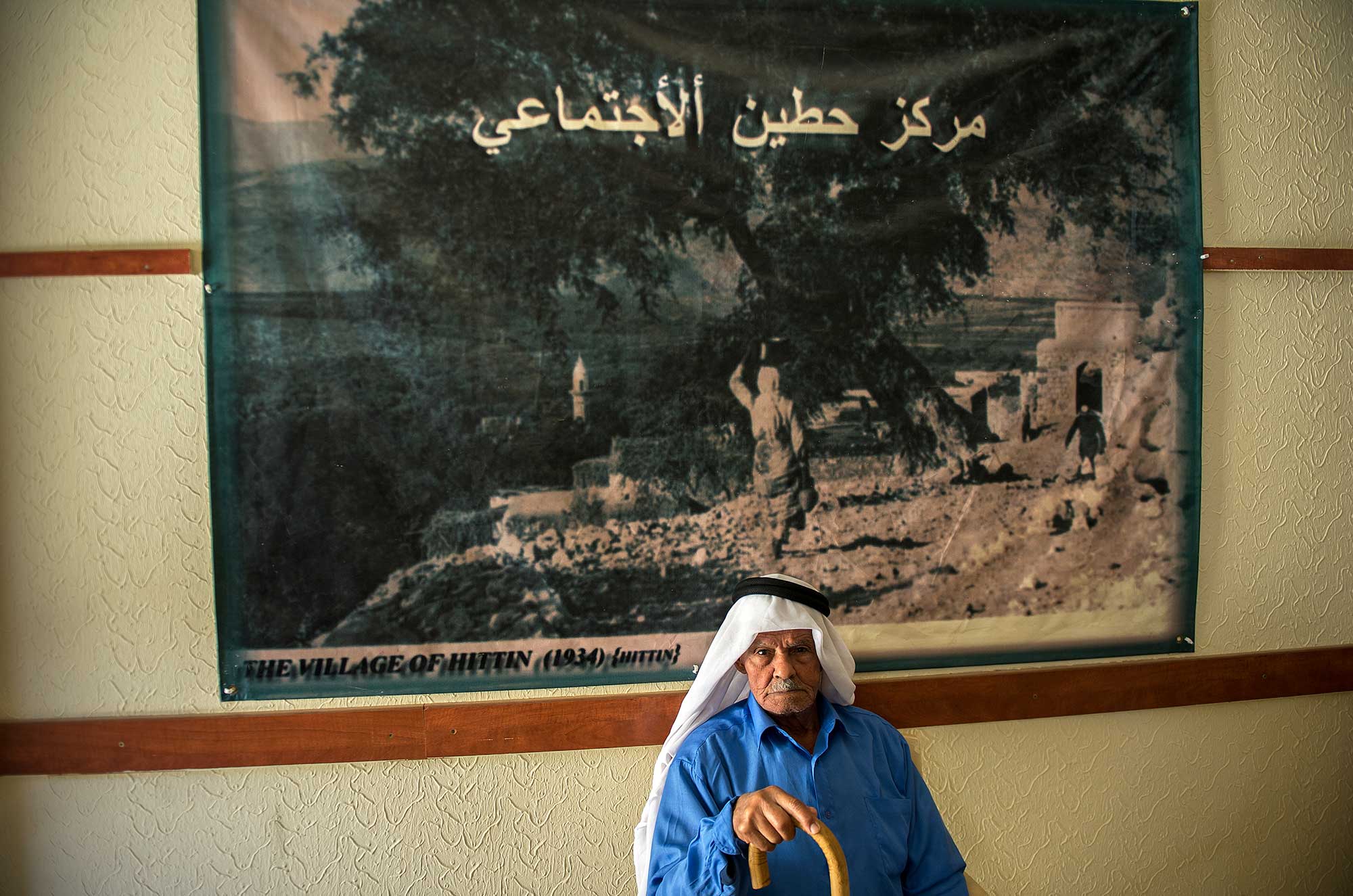 Palestinian refugee sitting in front of a picture of his home village of Hittin in northern Palestine
