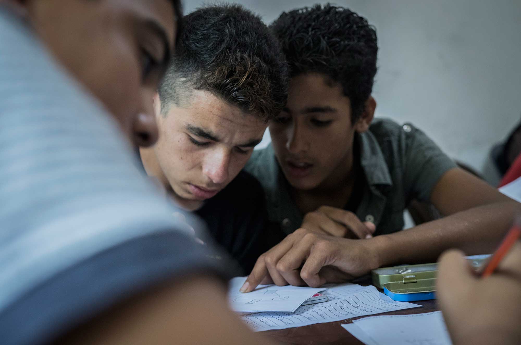 14-year-old Abed, a Syrian refugee, helps Hassan, who has been out of school for four years, with his classwork.