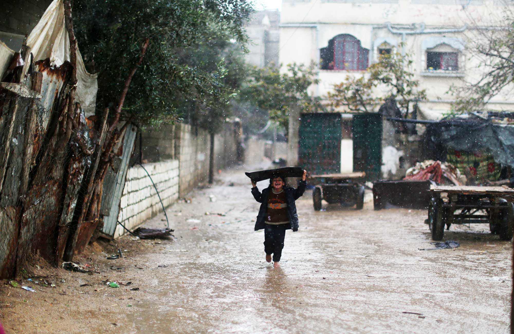 A Gaza child walks flooded streets with a board over her head, natural disasters are a problem as well as post conflict reconstruction.