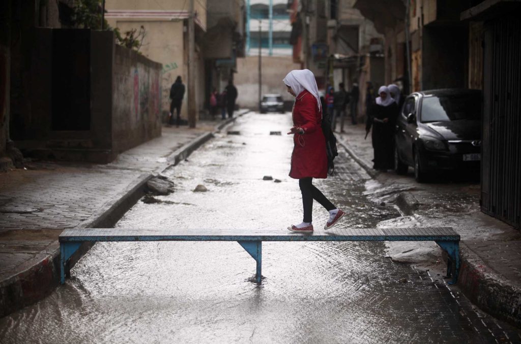 A Gaza woman walks across a plank over a flooded street. Natural disasters also factor in among post conflict reconstruction efforts.