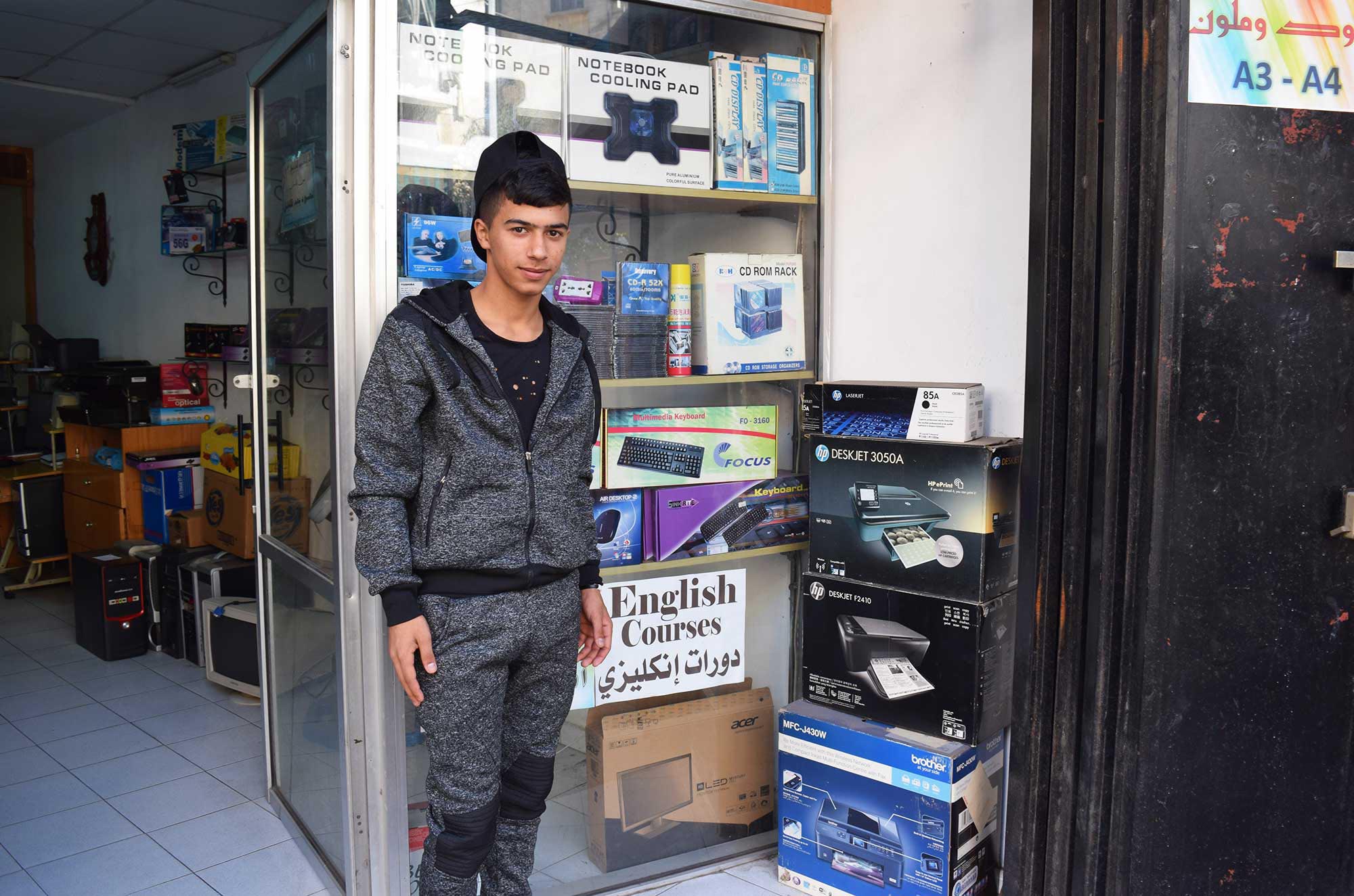 Khaled stands in front of the computer shop where he works.