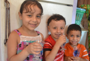 Three children happily sip clean, cold water Anera piped to their home on a hot summer day in Gaza.