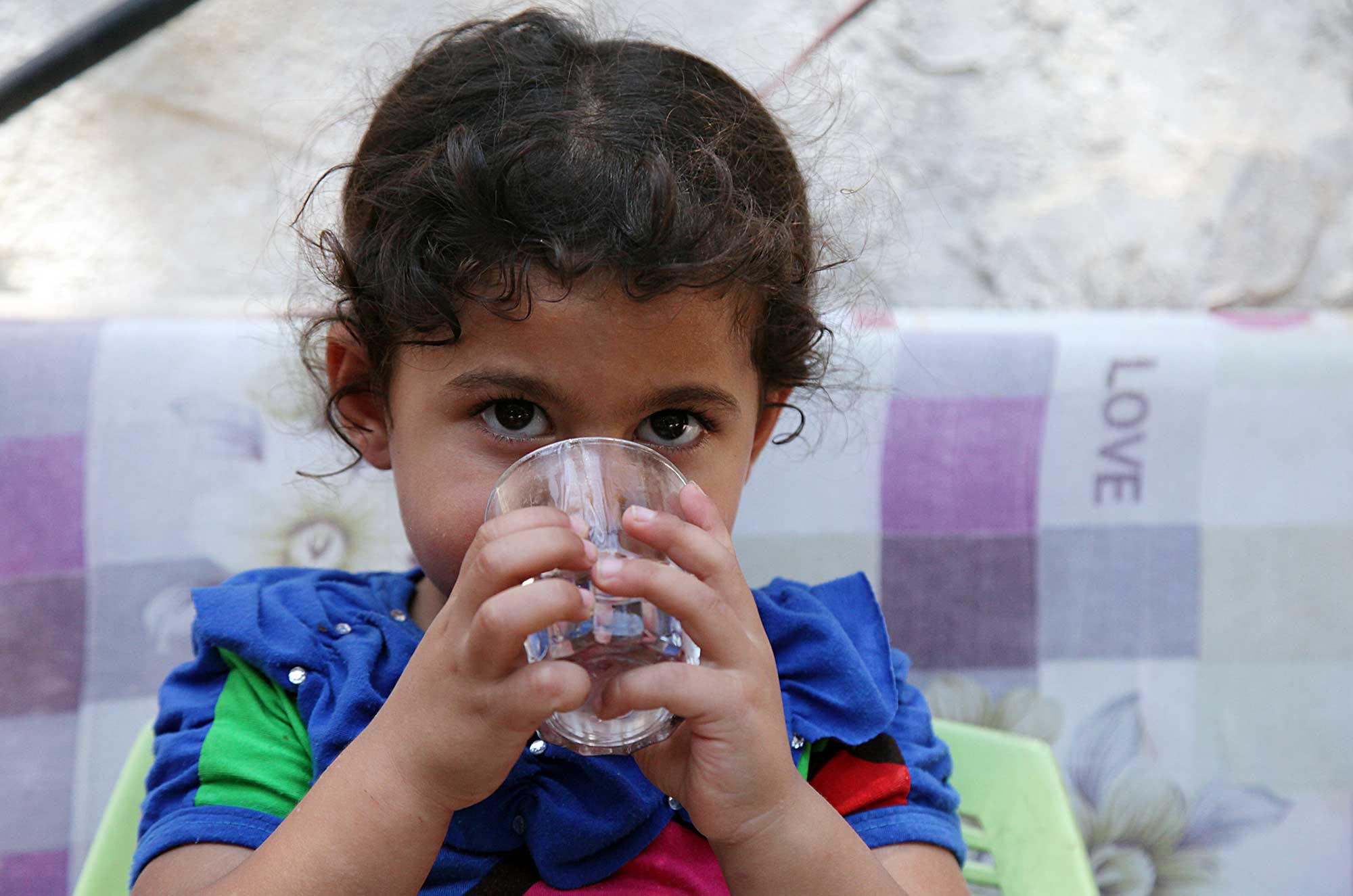 Rawda's daughter Mayar takes a sip from her cup of clean water.