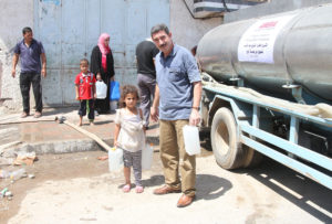 Nahed helps a young girl with her water jugs, just filled at an Anera tanker.