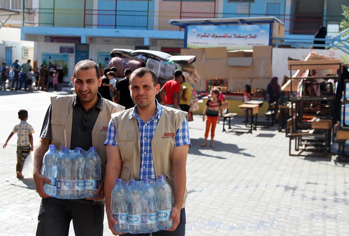 Anera staff members Sami Mater and Mohammad Ghossein deliver bottles of water to UN shelters for displaced Gaza families.