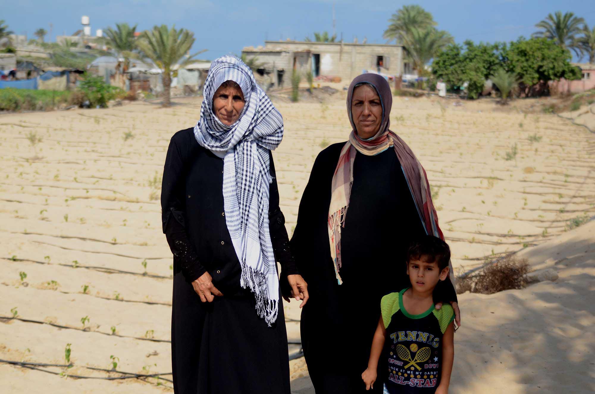 Fatima, Najat and Najat’s son stand in front of their field. Their home is in the background.