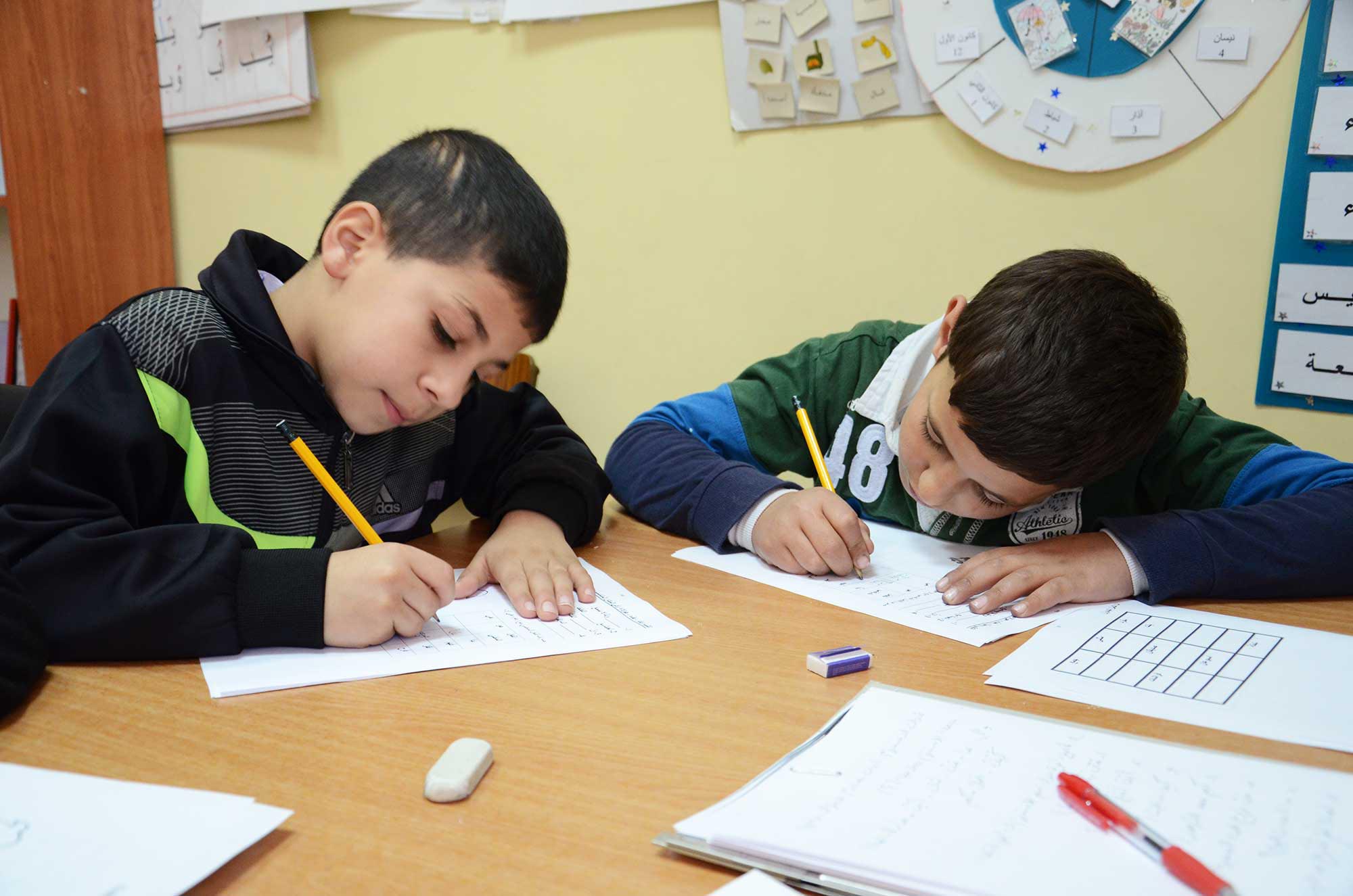 Two boys work on their activity sheets in the classroom. Small class sizes give the children more opportunities for individualized attention.