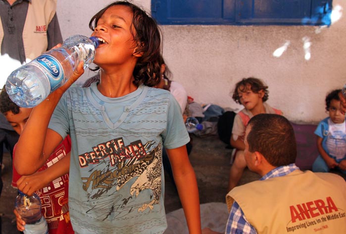 A young boy enjoys some water that Anera just delivered to the school where he and his family have been taking refuge.