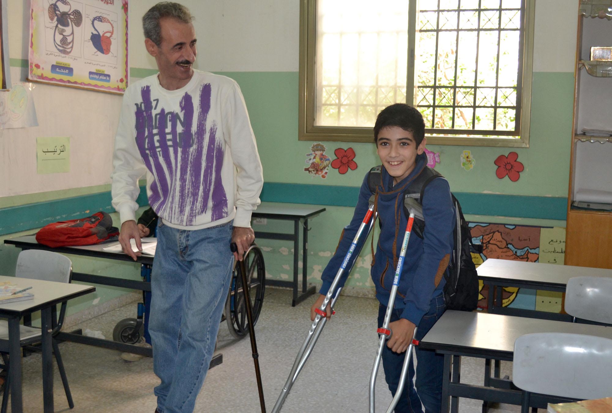 The director of Society for Handicapped in Gaza walks with his student, who now can move around more easily thanks to his new crutches from Anera.