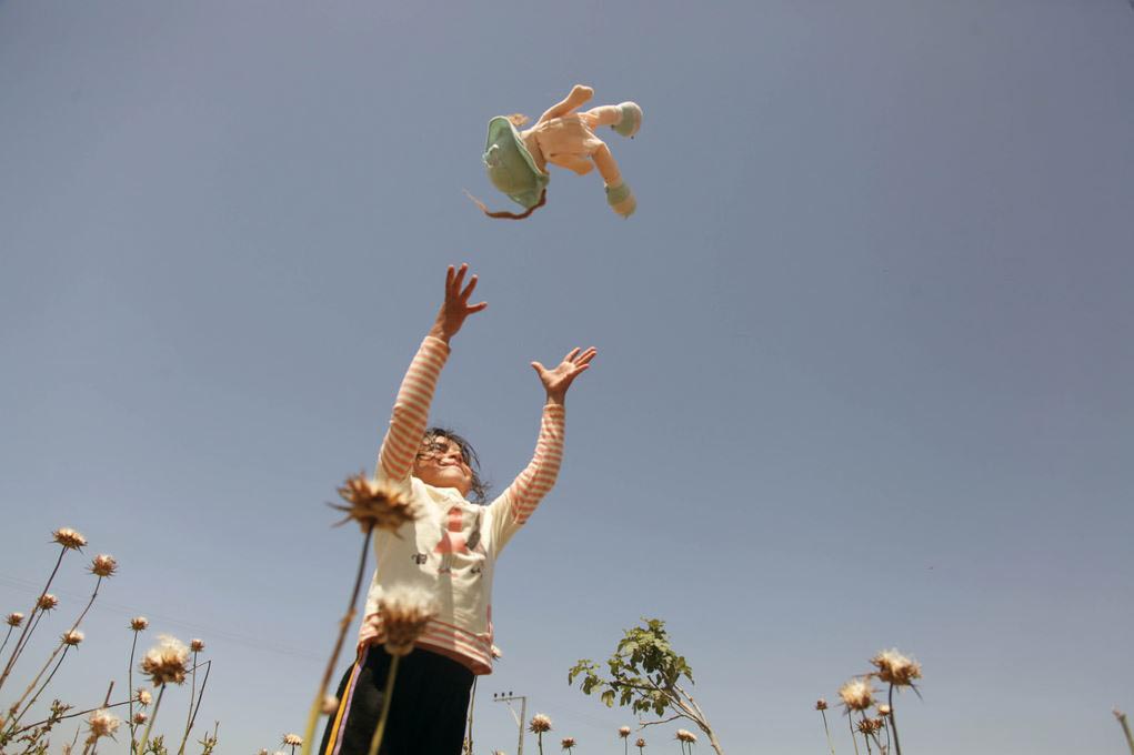 Palestinian girl throws her doll in the air in Gaza. Photo by Mohammed Zaanoun.