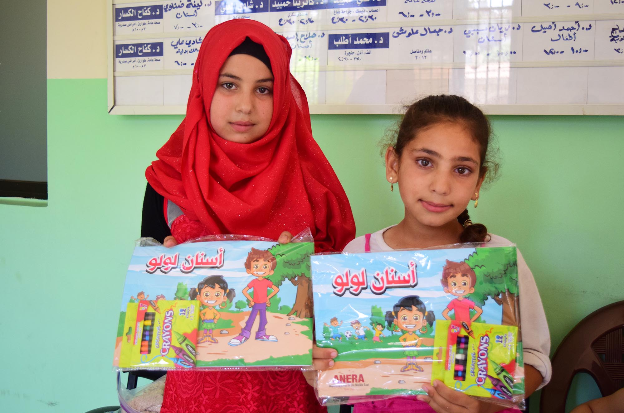 Dalaa and Shahed hold up activity booklets that teach refugee children how to care for their teeth.
