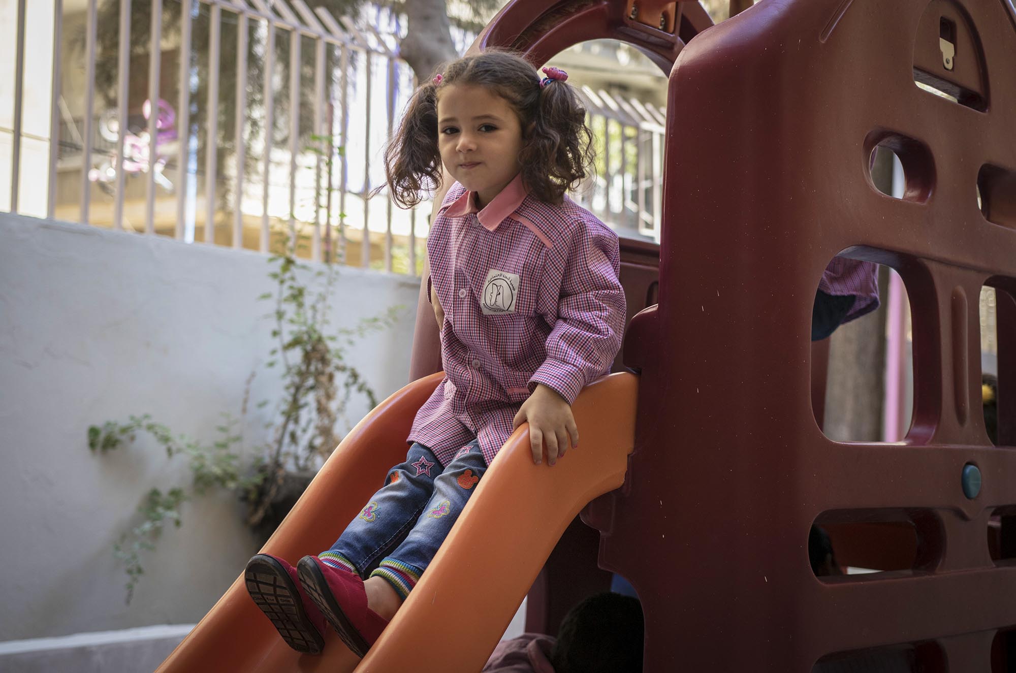 A refugee girl in Beddawi Camp in Lebanon plays in the playground of her school with brand new TOMS shoes.