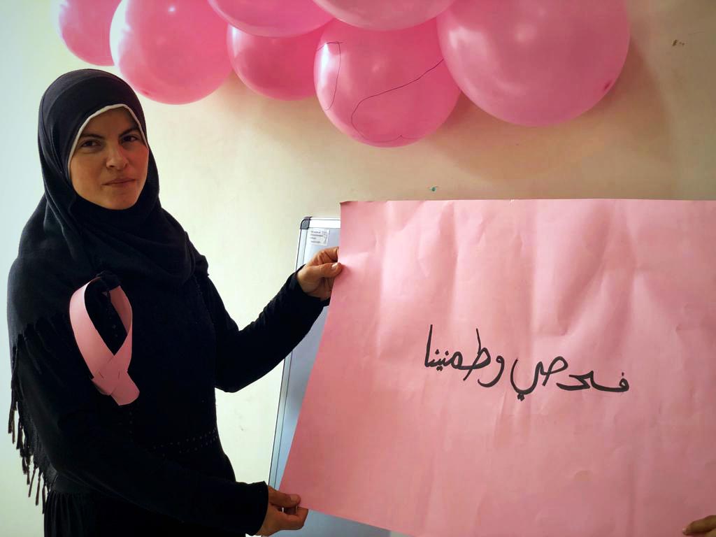 Amina in class next to a banner on which she written a public health message.