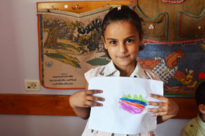 A young Palestinian girl in Gaza shows off her artwork that she made during an Anera summer camp.