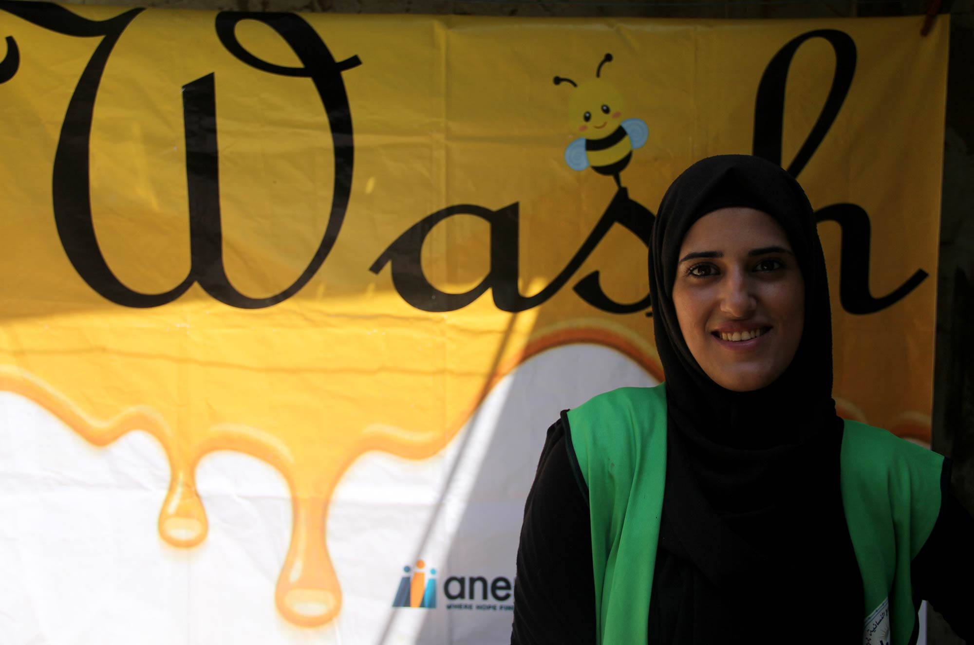 Lilian in Burj El Barajneh stands in front of an Anera WASH banner.