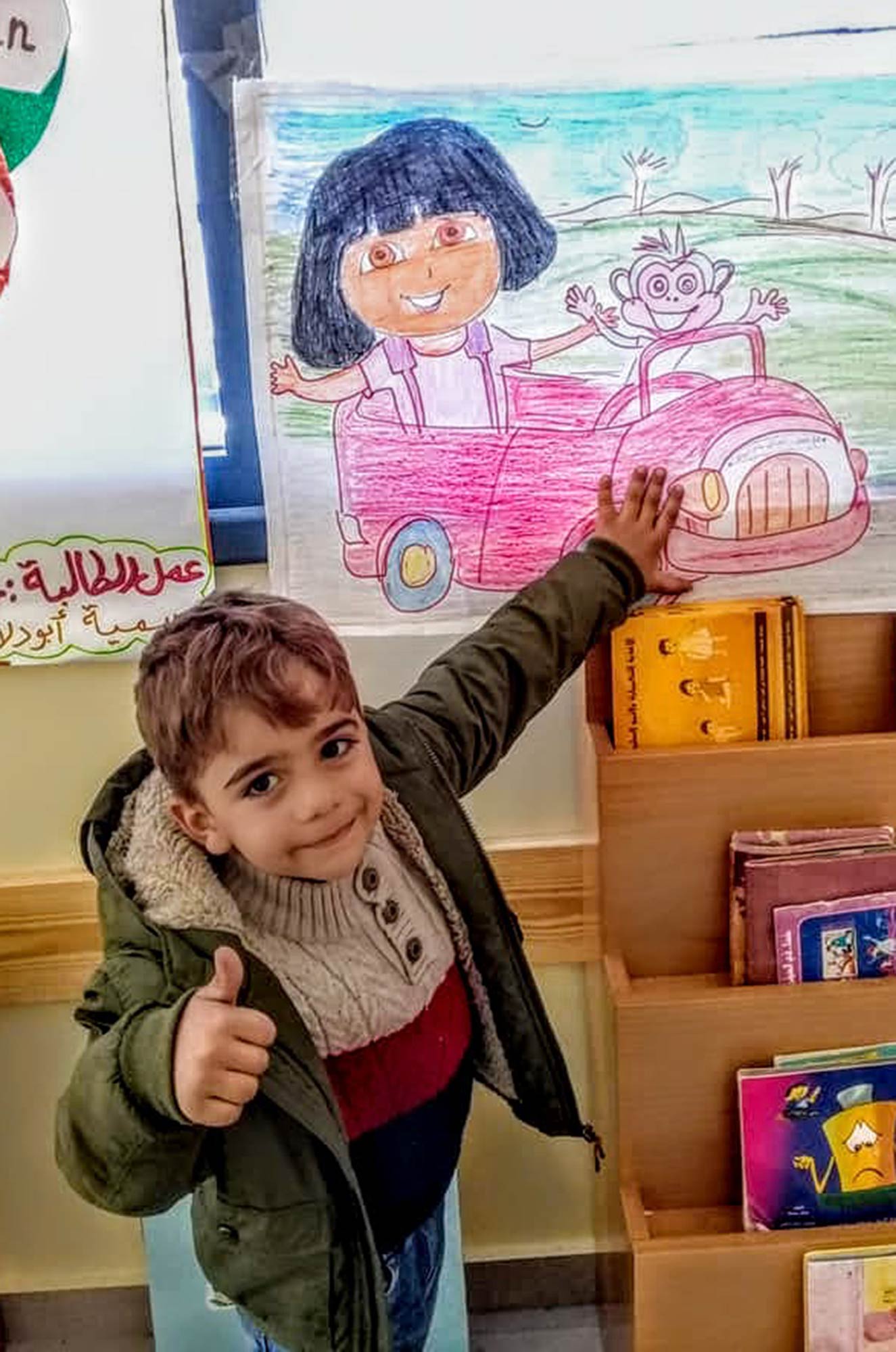 A new preschool in Gaza’s Nuseirat Refugee Camp, boy with Dora the Explorer A preschooler poses in front of Dora the Explorer in his new preschool.