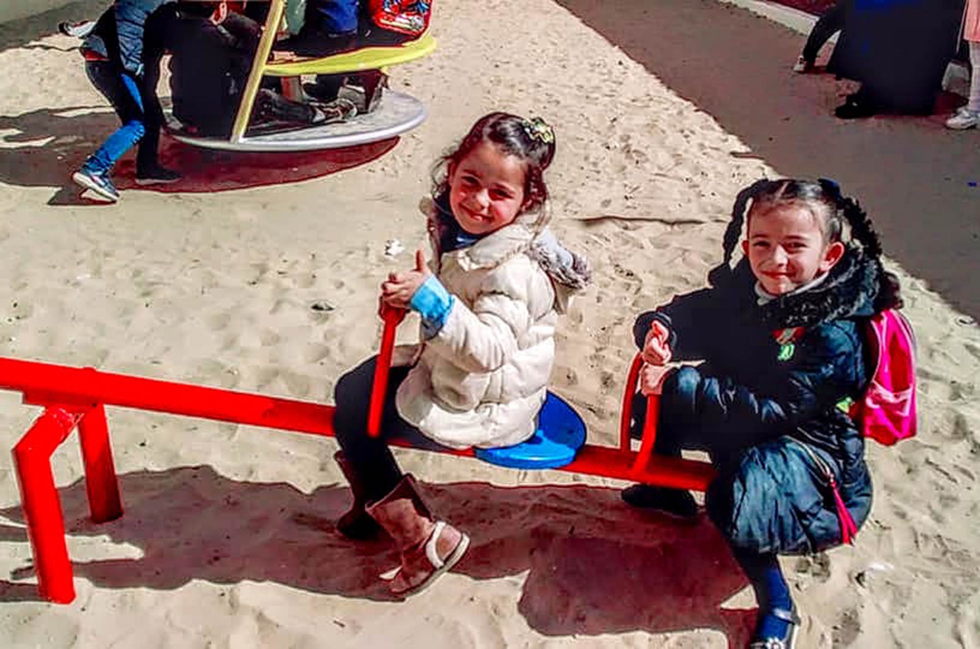 Two girls are enjoying the seesaw in the playground of their newly built preschool.