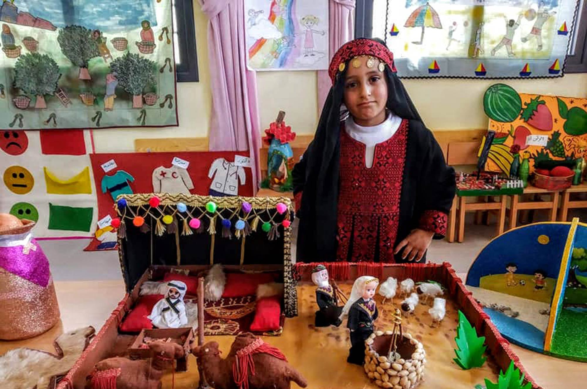 A new preschool for refugee children in Nusairat, Gaza, girl sporting a thobe A preschooler in a thobe shows off a diorama