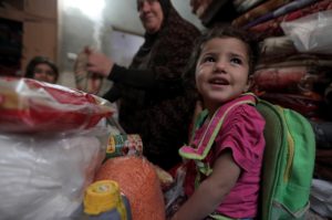 A young girl smiles while sitting next ot heaps of lentils and other food parcel ingredients