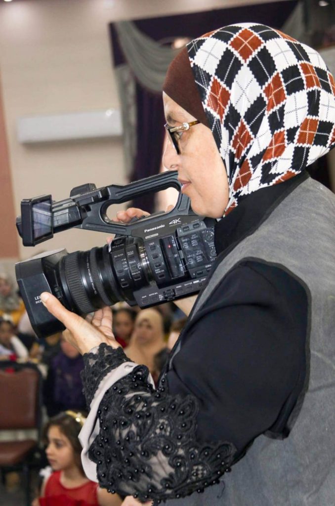 Manal holds a video camera, filming a local wedding.