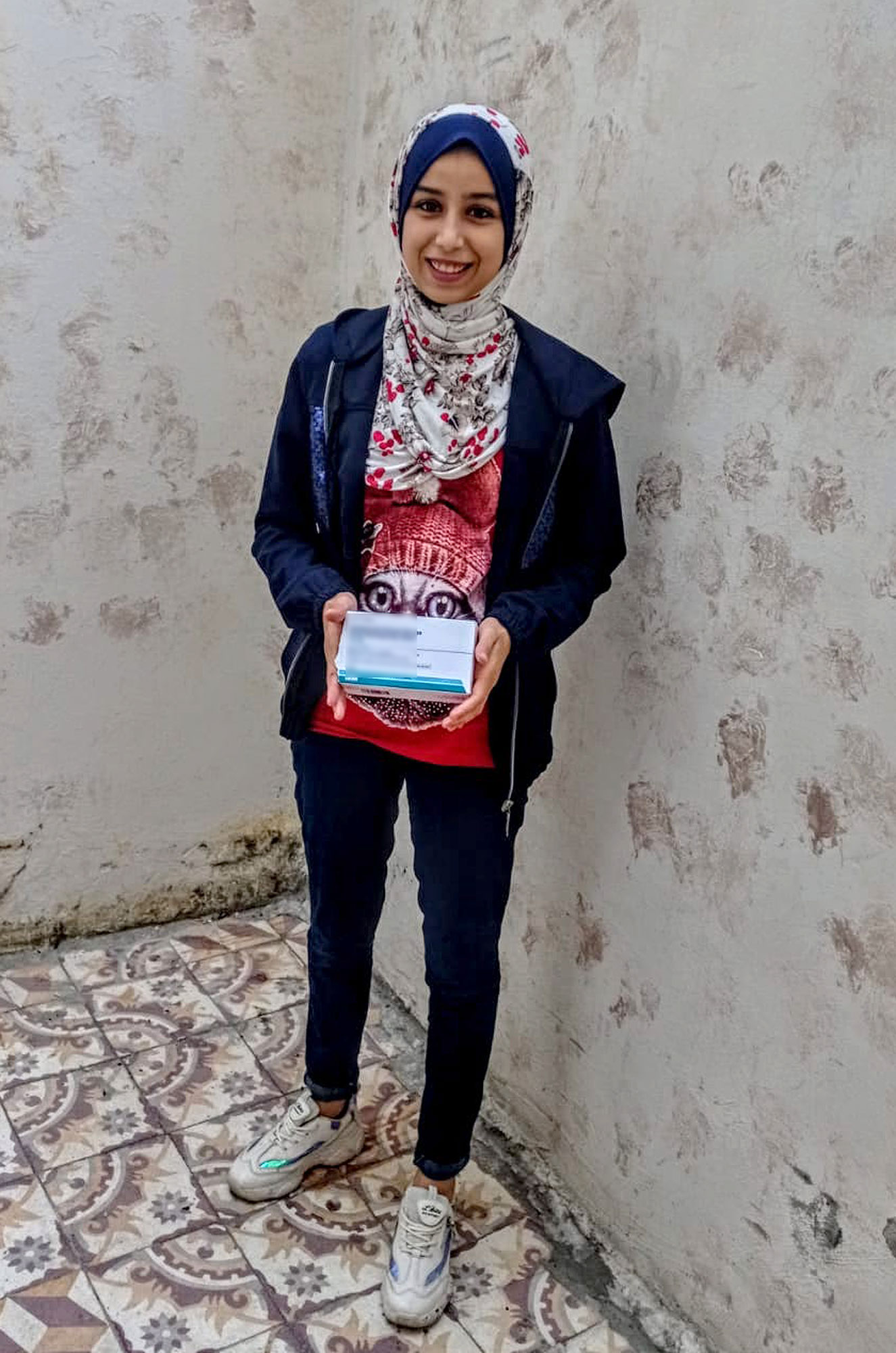 Haya holds a box of her medication.