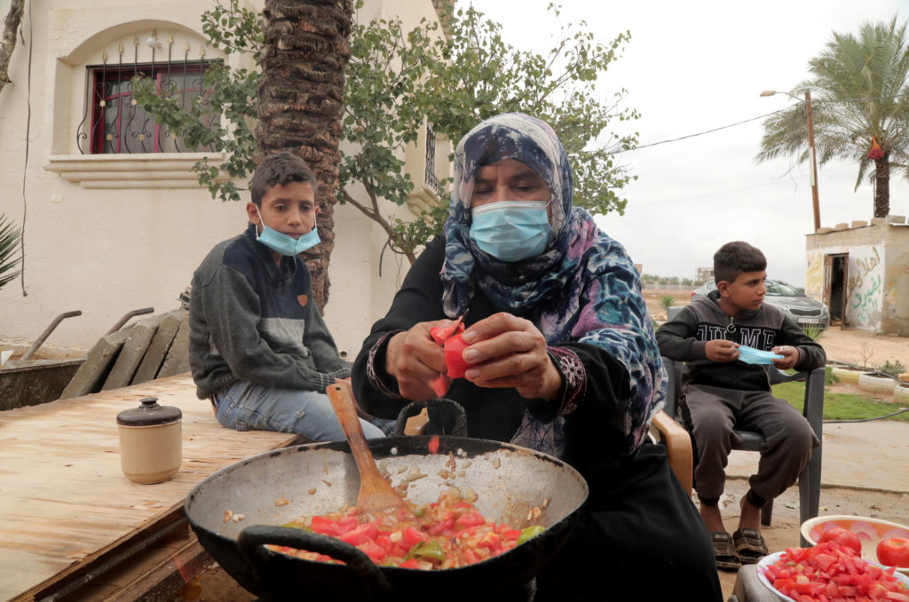 Halima chops tomatoes into a wok over an outdoor stove.