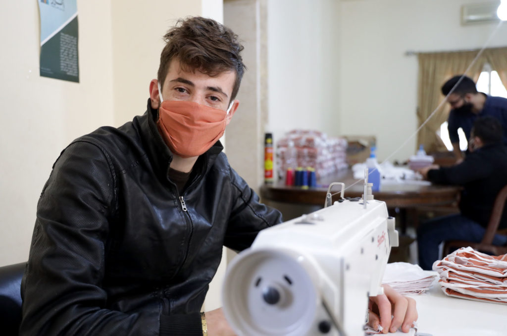 Vocational sewing student at his machine making masks.