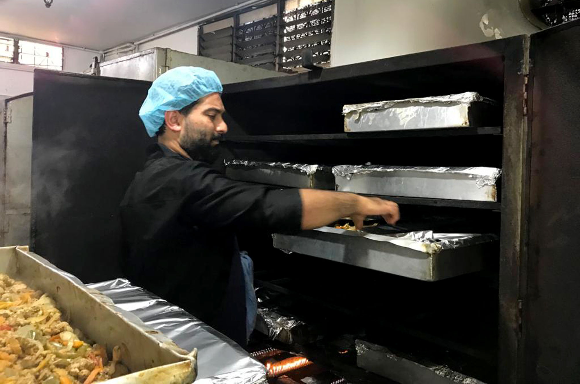 A man checks on food trays in a large restaurant oven.