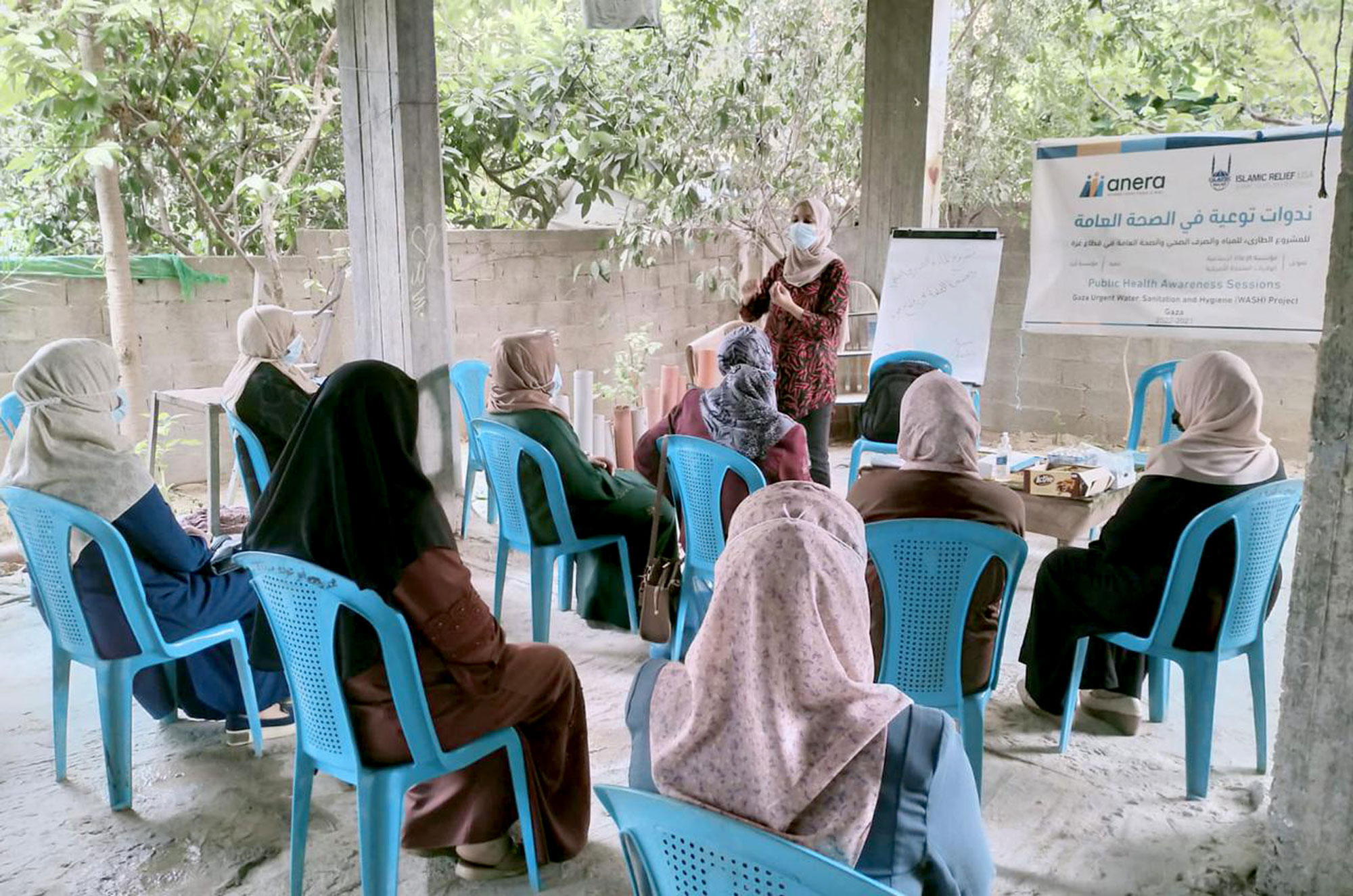 A woman presents to a group of seated women outdoors.