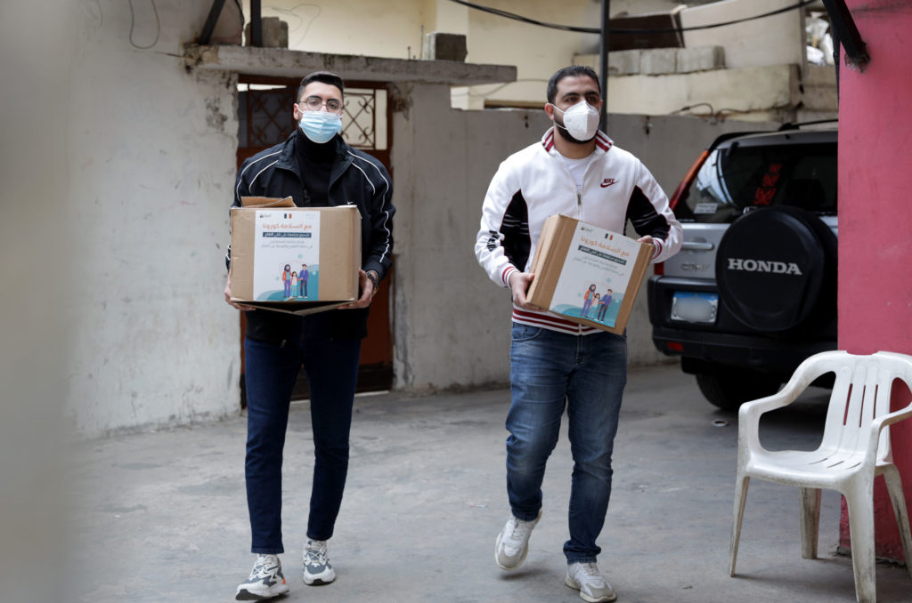 Two Anera volunteers carry food and hygiene boxes.