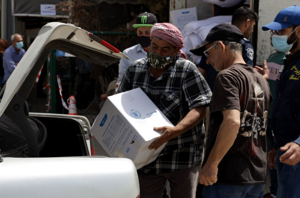 Families collect parcels of food at a distribution center.