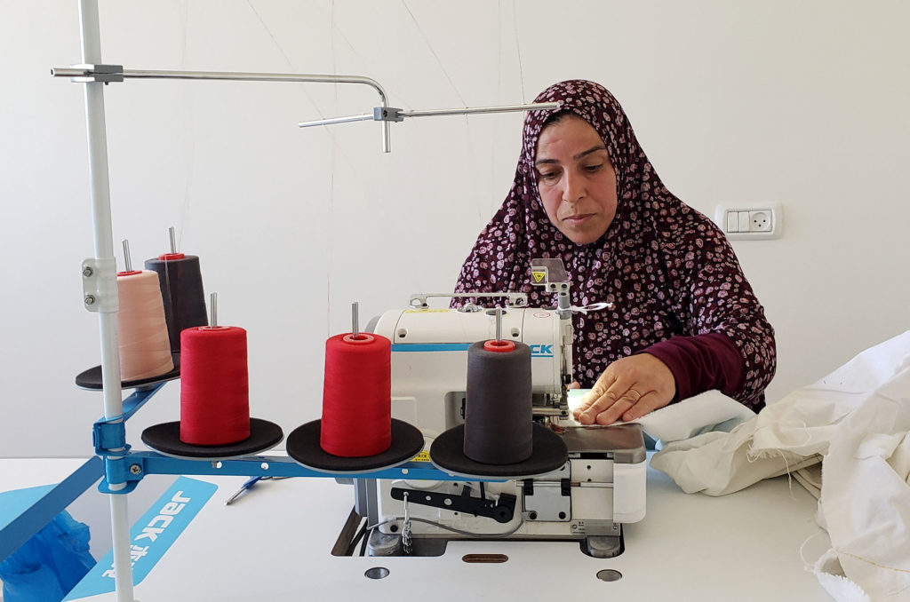 Fatima working at her new sewing machine with spools of thread.